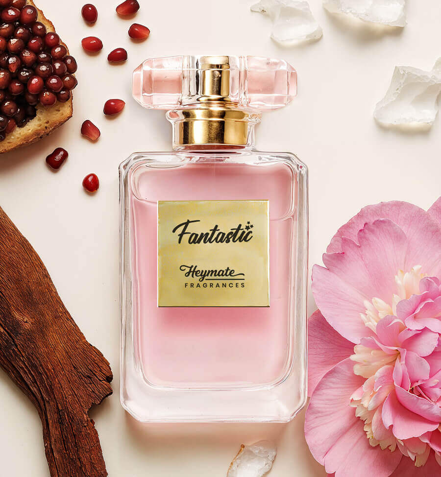 Pink perfume bottle labeled 'Fantastic' by Heymate Fragrances with flowers and pomegranate seeds on a light background.