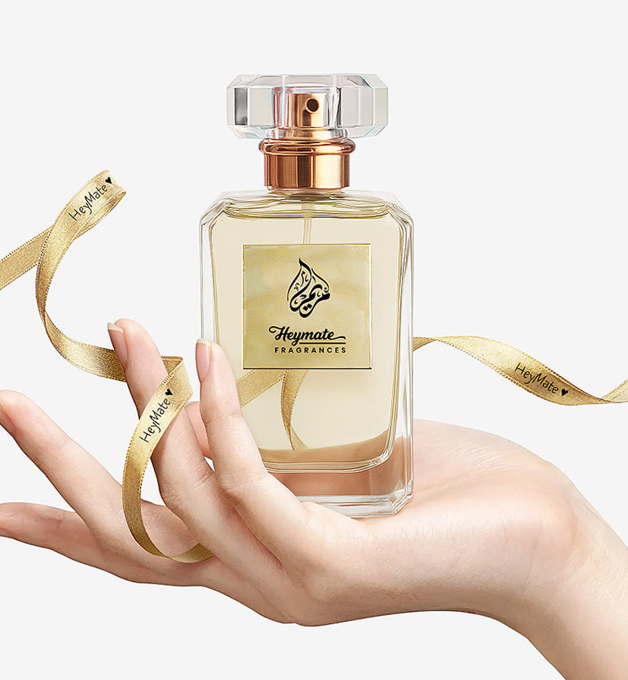 Perfume bottle held by a hand with gold ribbon, featuring Heymate Fragrances branding.