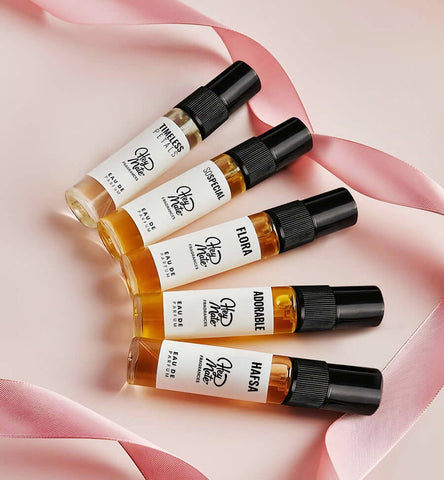 Five small perfume bottles with labels on a pink fabric background